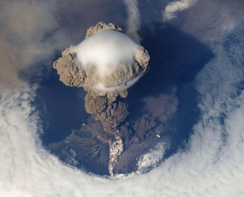 volcano erupting with ash cloud over island coast